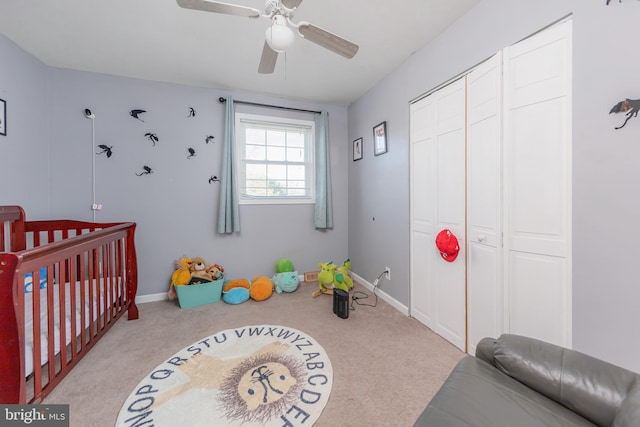 bedroom featuring a closet, a nursery area, light carpet, and ceiling fan