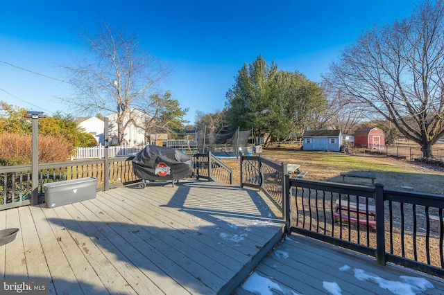 wooden terrace featuring a yard, a grill, a storage shed, and a trampoline