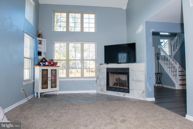 unfurnished living room featuring baseboards, a tile fireplace, a high ceiling, stairs, and dark carpet