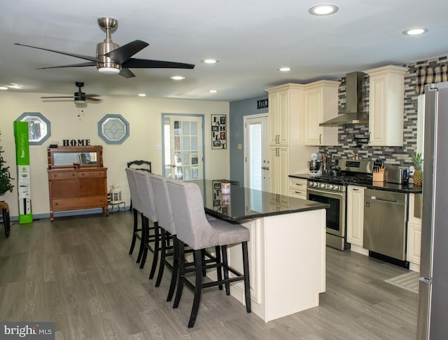 kitchen with dark wood-style floors, stainless steel appliances, a kitchen island, dark stone countertops, and wall chimney exhaust hood