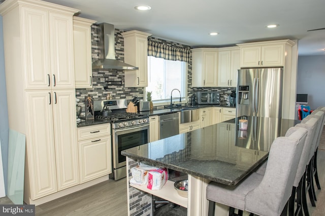 kitchen featuring appliances with stainless steel finishes, cream cabinetry, wall chimney range hood, and a kitchen breakfast bar