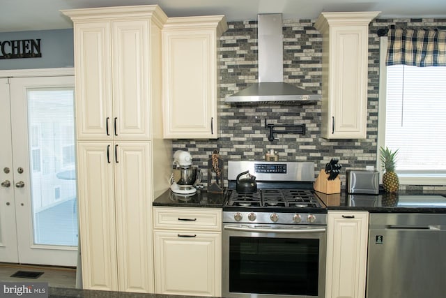 kitchen with cream cabinetry, stainless steel gas stove, backsplash, and wall chimney exhaust hood