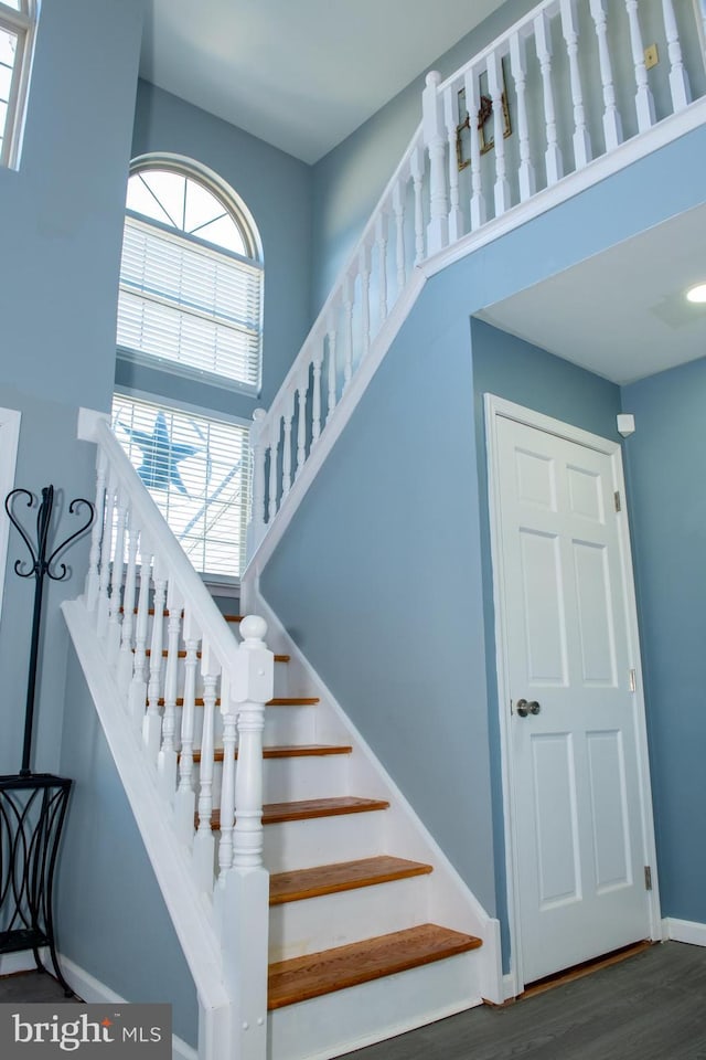 stairway with a towering ceiling, baseboards, and wood finished floors