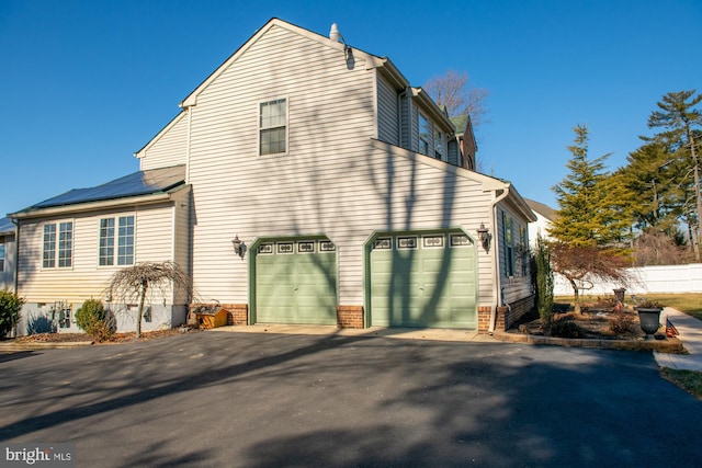 view of side of home with a garage, aphalt driveway, and solar panels