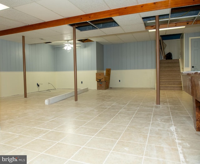 finished below grade area featuring stairs, a drop ceiling, and light tile patterned floors