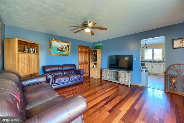 living room featuring wood-type flooring, ceiling fan with notable chandelier, and a textured ceiling