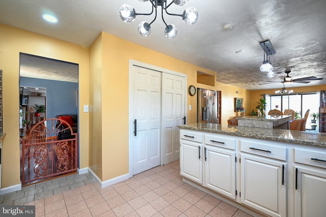 kitchen with light tile patterned floors, hanging light fixtures, light stone counters, white cabinets, and ceiling fan with notable chandelier