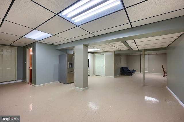 basement with stainless steel fridge with ice dispenser and a paneled ceiling