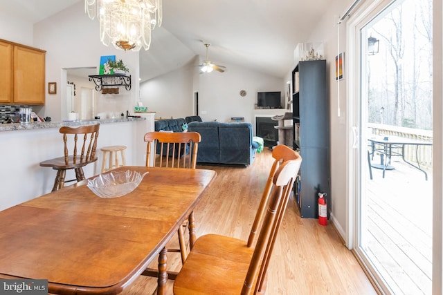 dining room with vaulted ceiling, ceiling fan with notable chandelier, and light wood-type flooring