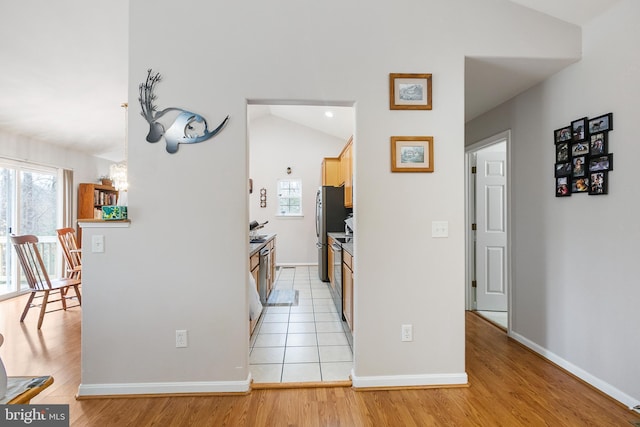 kitchen with appliances with stainless steel finishes, light brown cabinetry, vaulted ceiling, and light hardwood / wood-style flooring