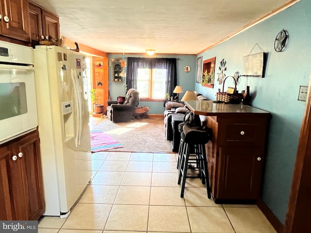 kitchen featuring white appliances, light tile patterned flooring, crown molding, and a kitchen bar