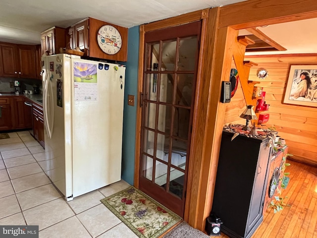 kitchen featuring white refrigerator with ice dispenser, wood walls, and light tile patterned floors