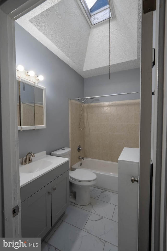 full bathroom featuring a skylight, a textured ceiling, toilet, vanity, and tiled shower / bath