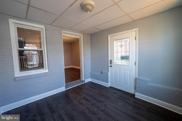 foyer entrance featuring a paneled ceiling, dark hardwood / wood-style floors, and brick wall