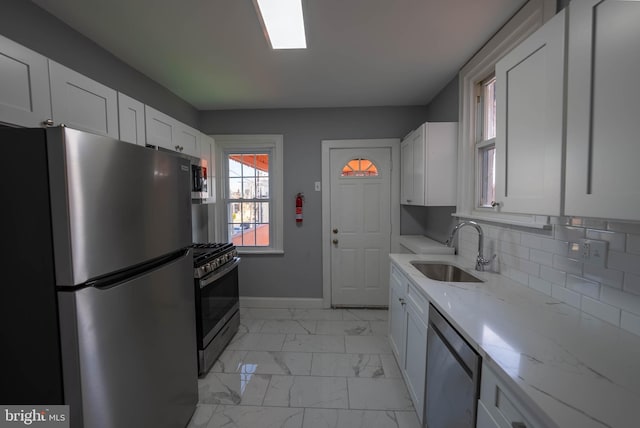 kitchen with light stone countertops, white cabinetry, sink, and appliances with stainless steel finishes