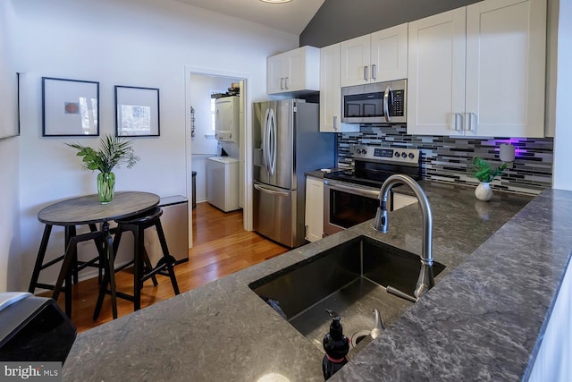 kitchen featuring white cabinetry, appliances with stainless steel finishes, stacked washing maching and dryer, and sink