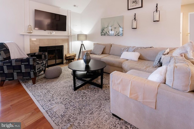 living room featuring a tile fireplace, vaulted ceiling, and light hardwood / wood-style flooring