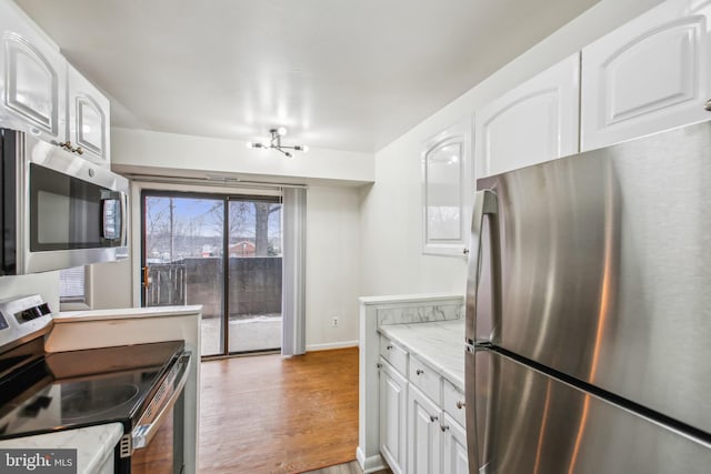 kitchen with light stone countertops, white cabinetry, appliances with stainless steel finishes, and light wood-type flooring