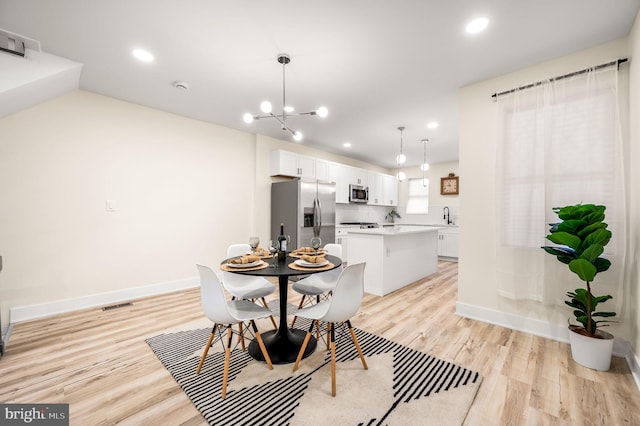 dining area with light wood-type flooring, a notable chandelier, and sink