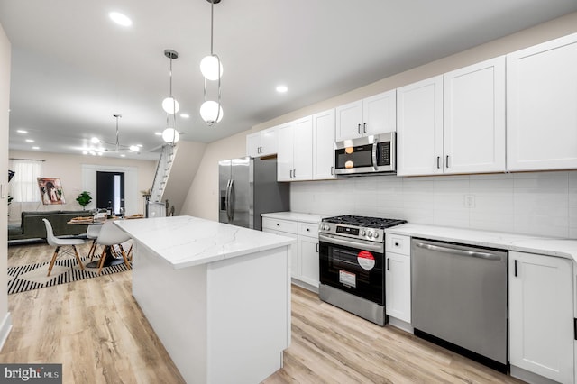 kitchen featuring pendant lighting, backsplash, white cabinets, appliances with stainless steel finishes, and a kitchen island