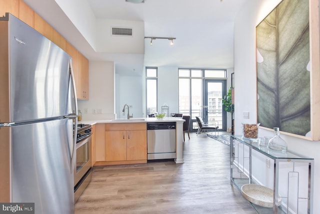 kitchen with appliances with stainless steel finishes, kitchen peninsula, expansive windows, sink, and light hardwood / wood-style flooring