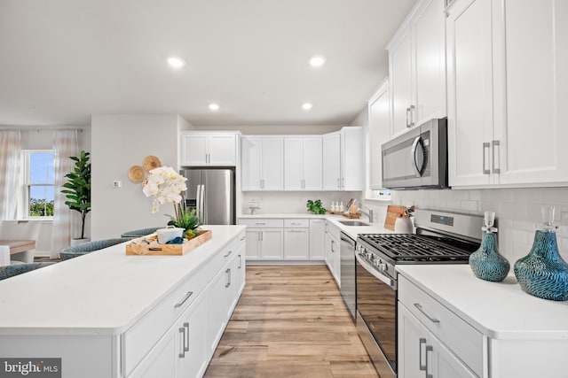 kitchen featuring decorative backsplash, a kitchen island, white cabinets, appliances with stainless steel finishes, and sink