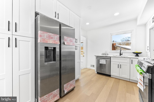 kitchen with appliances with stainless steel finishes, light hardwood / wood-style flooring, white cabinetry, and sink