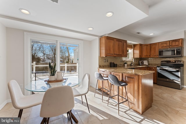 kitchen featuring kitchen peninsula, stainless steel appliances, light stone countertops, and a wealth of natural light