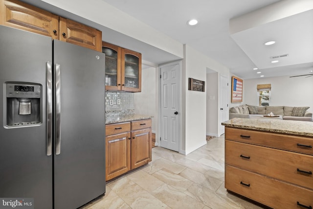 kitchen with ceiling fan, stainless steel fridge with ice dispenser, backsplash, and light stone countertops