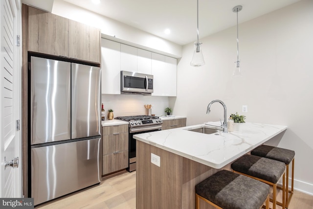 kitchen featuring light stone countertops, hanging light fixtures, white cabinets, appliances with stainless steel finishes, and sink