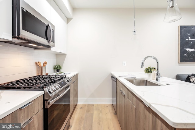 kitchen with sink, white cabinetry, light wood-type flooring, hanging light fixtures, and appliances with stainless steel finishes