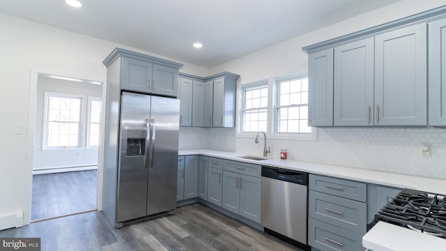 kitchen featuring dark wood-type flooring, tasteful backsplash, a baseboard heating unit, appliances with stainless steel finishes, and sink