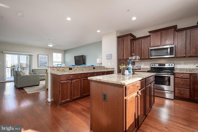 kitchen with light stone counters, ceiling fan, a kitchen island, dark hardwood / wood-style flooring, and appliances with stainless steel finishes