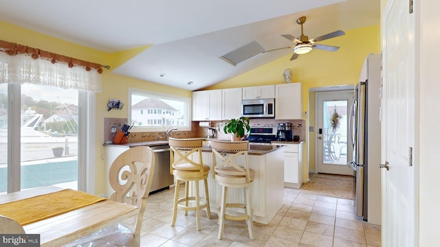 kitchen featuring stainless steel appliances, white cabinets, a center island, vaulted ceiling, and a kitchen bar