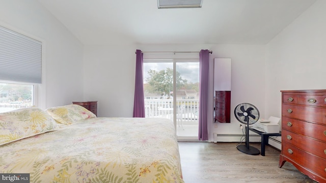 bedroom featuring a baseboard heating unit, access to exterior, multiple windows, and light hardwood / wood-style flooring