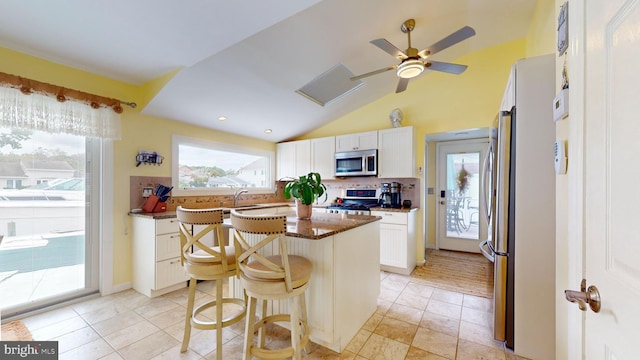 kitchen with stainless steel appliances, a kitchen island, lofted ceiling, white cabinetry, and a kitchen breakfast bar