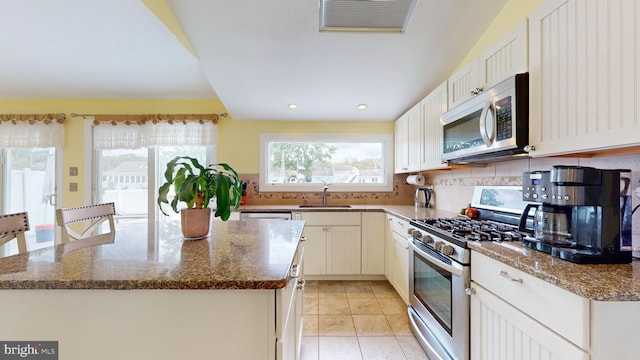 kitchen with white cabinets, stainless steel appliances, dark stone counters, a kitchen island, and sink