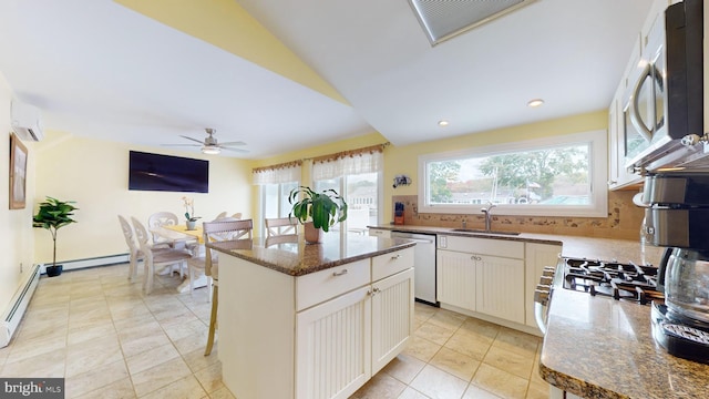 kitchen featuring dark stone countertops, stainless steel appliances, a center island, ceiling fan, and sink