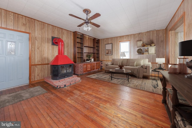 living room with built in shelves, ceiling fan, light hardwood / wood-style floors, and a wood stove