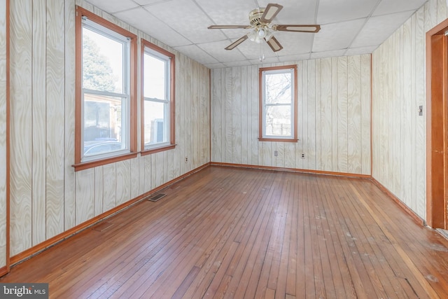 empty room featuring a paneled ceiling, wooden walls, ceiling fan, and light hardwood / wood-style floors