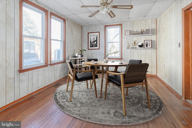 dining room featuring a paneled ceiling, wood-type flooring, wood walls, and ceiling fan