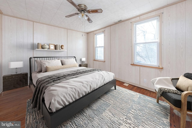 bedroom with ceiling fan, wooden walls, and hardwood / wood-style floors