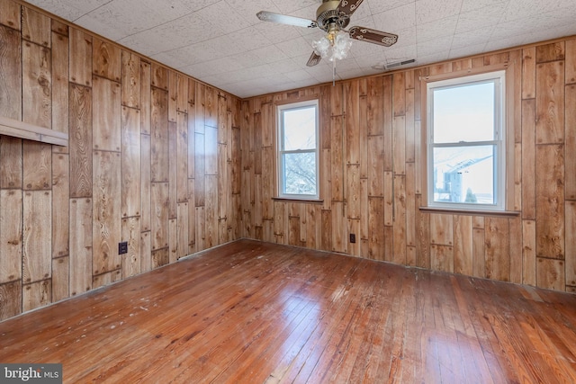 empty room with wood-type flooring, wooden walls, and ceiling fan