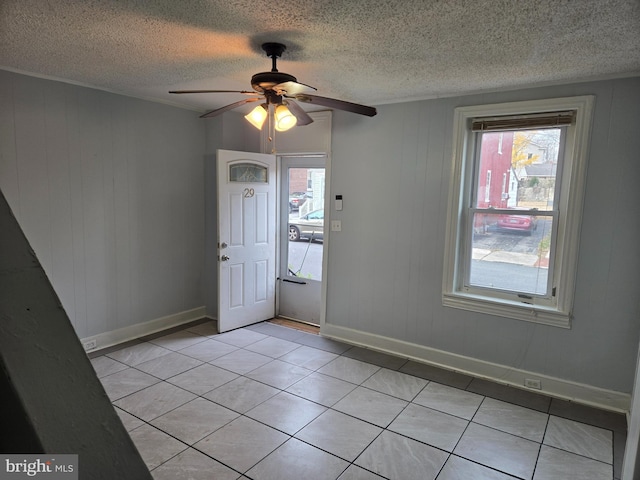 entrance foyer with ceiling fan, wood walls, light tile patterned flooring, and a textured ceiling