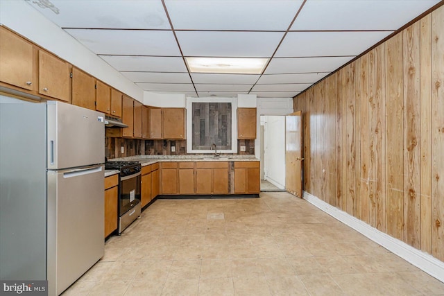 kitchen featuring appliances with stainless steel finishes, backsplash, wood walls, and sink