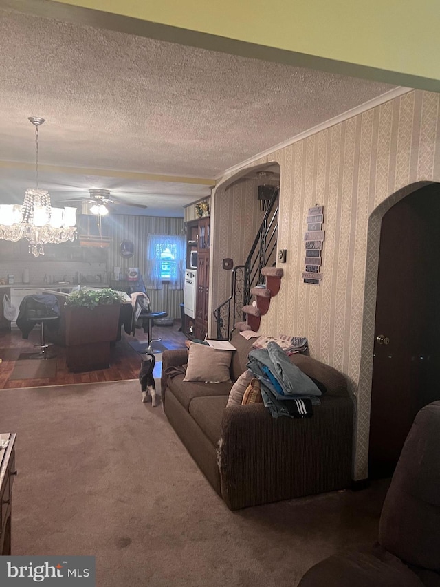 living room featuring ceiling fan with notable chandelier, a textured ceiling, carpet, and crown molding