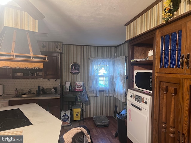 kitchen featuring cooktop, sink, stacked washer and clothes dryer, a textured ceiling, and ventilation hood