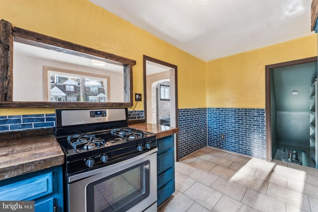 kitchen with stainless steel gas stove, plenty of natural light, light tile patterned floors, and tile walls