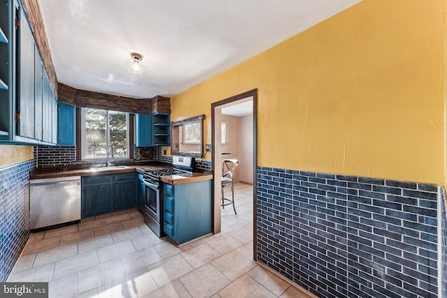 kitchen with dishwasher, sink, blue cabinetry, light tile patterned floors, and stainless steel range with gas stovetop