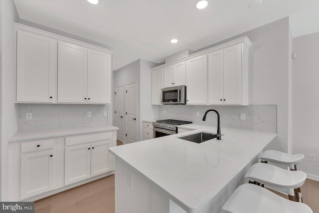 kitchen with sink, a breakfast bar, stainless steel appliances, white cabinets, and kitchen peninsula